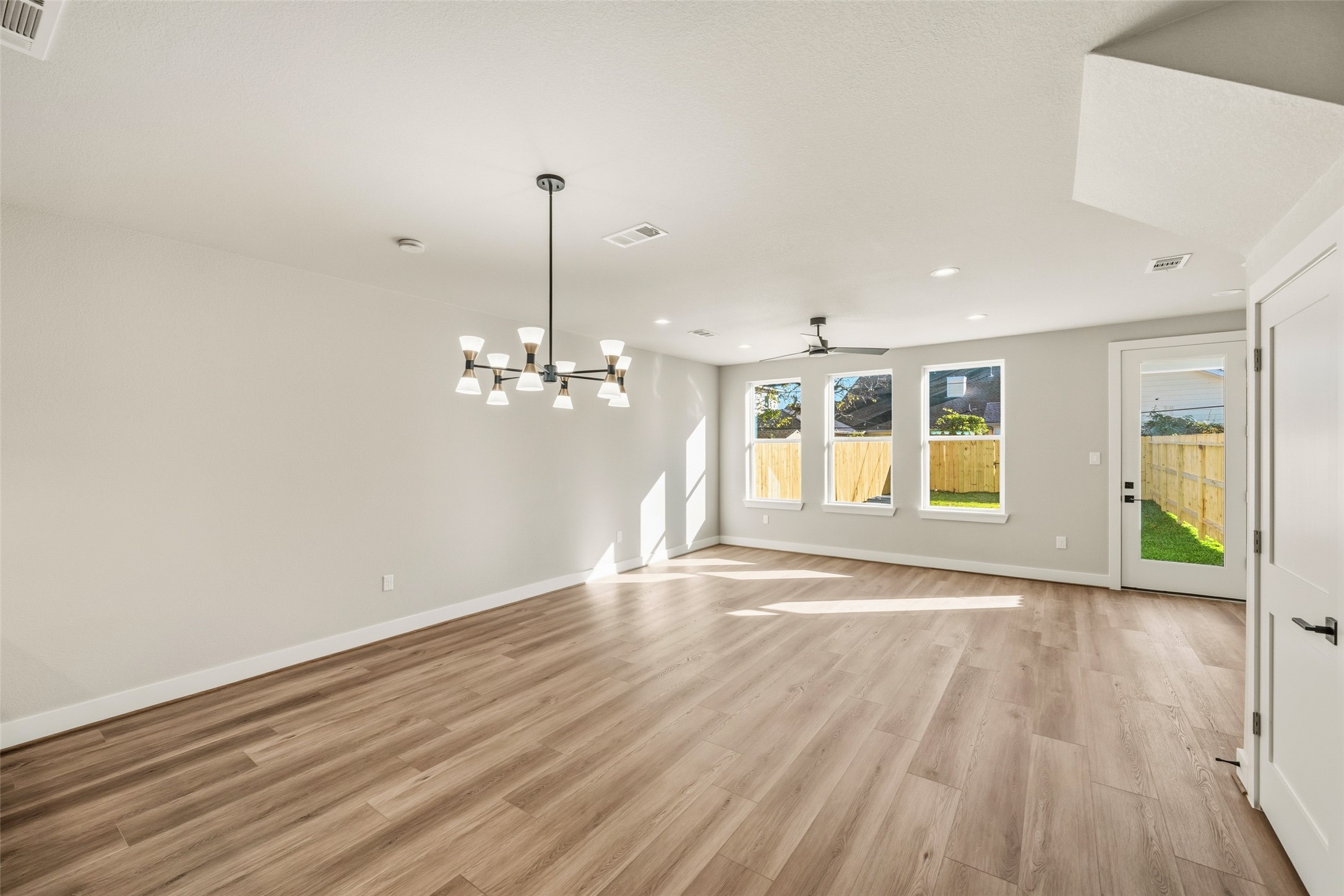 3422 Elser Street Houston, TX 77009 - Photo 5 of 26 This spacious living area features modern wood flooring, neutral walls, and large windows that provide ample natural light. A stylish chandelier and ceiling fan enhance the room, while a door leads to a fenced backyard, perfect for indoor-outdoor living.