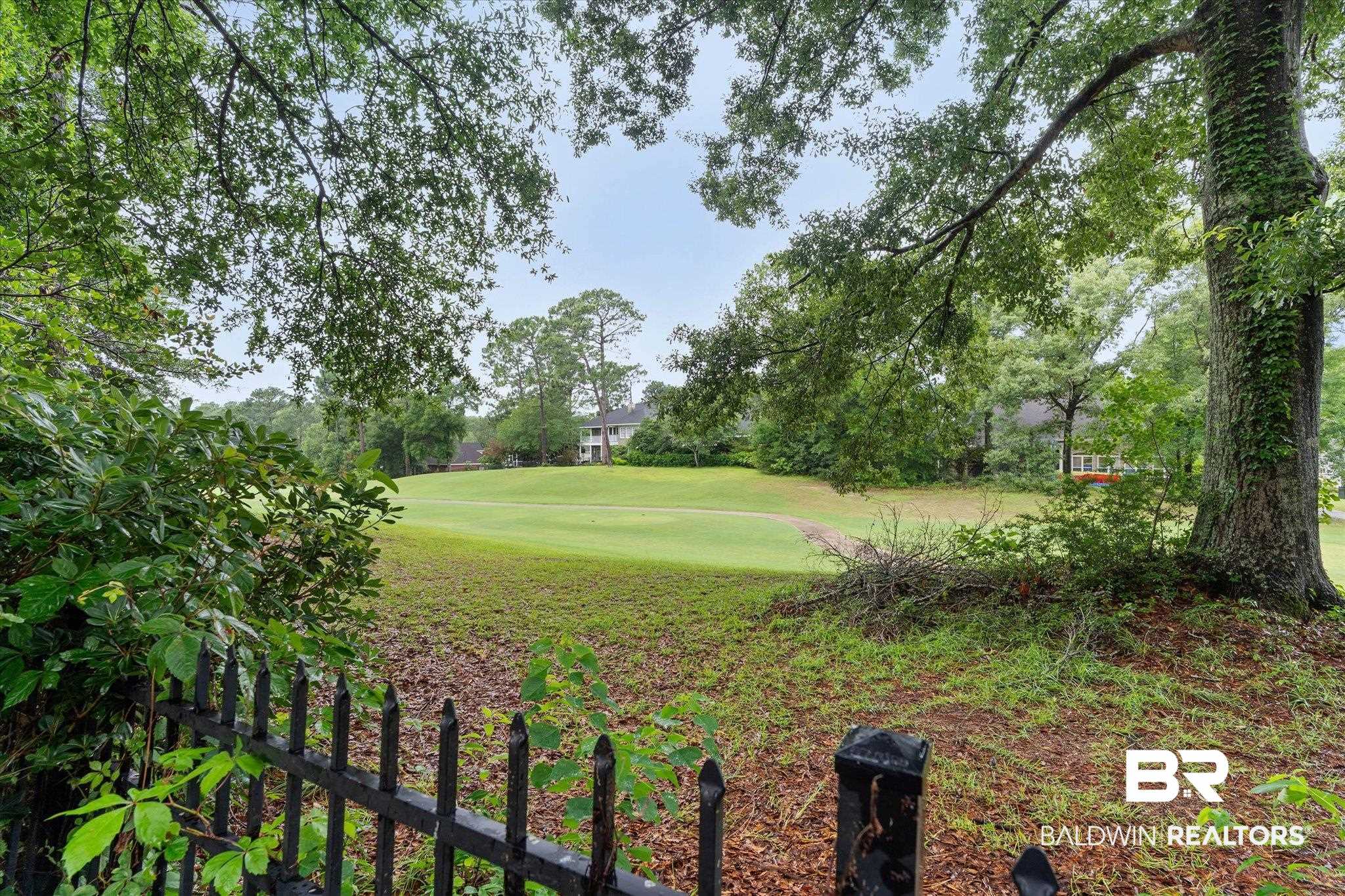 136 Old Mill Road Fairhope, AL 36532 - Photo 31 of 36 Expansive green space featuring a sloped lawn, mature trees, and a black wrought iron fence