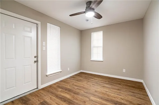 an empty room with wooden floor chandelier fan and windows