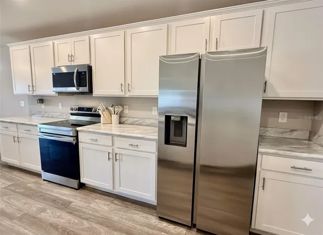 a kitchen with stainless steel appliances granite countertop a refrigerator stove and white cabinets