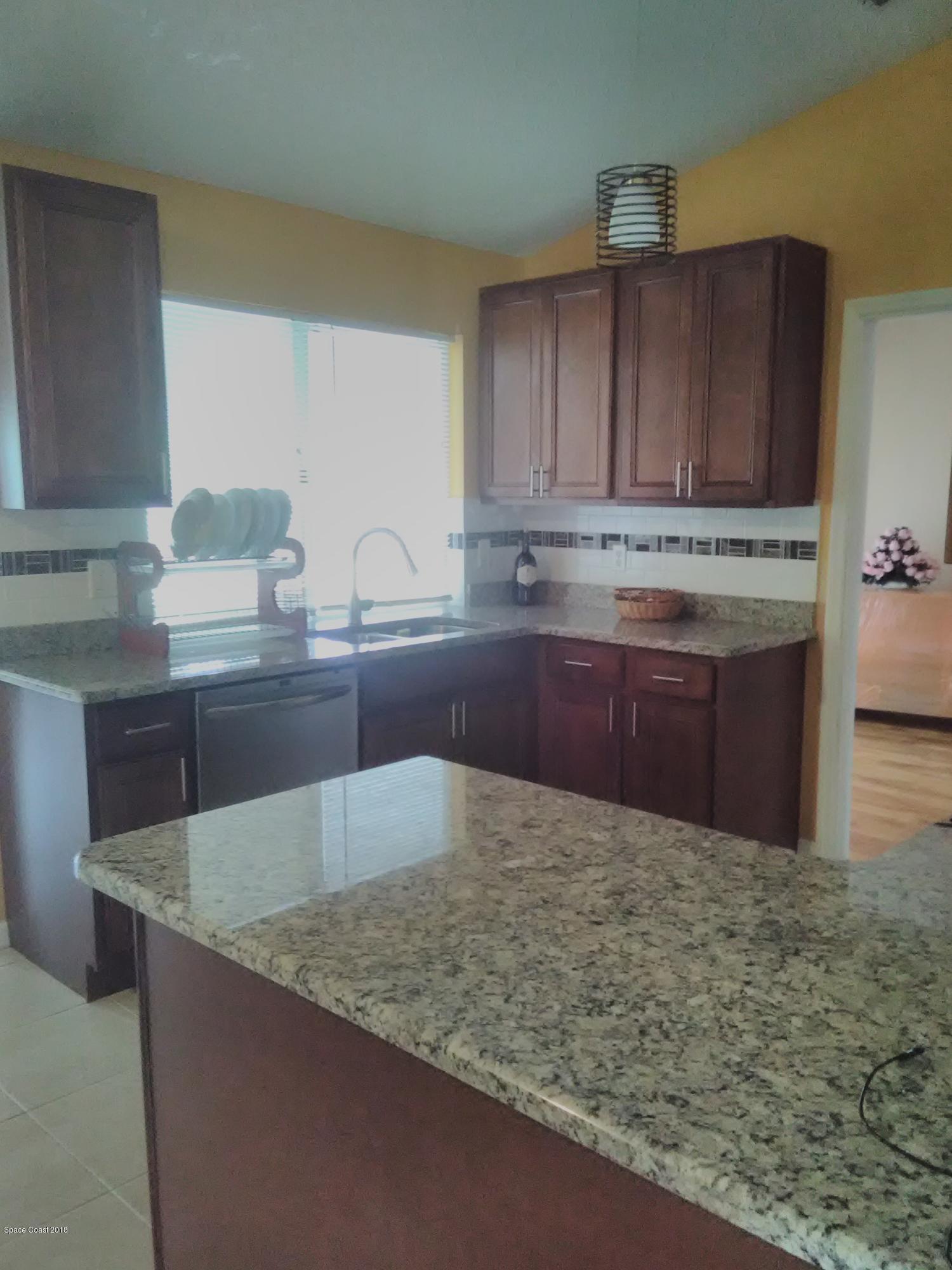 231 Rheine Road Northwest Palm Bay, FL 32907 - Photo 5 of 10 a kitchen with kitchen island granite countertop a sink and a wooden cabinets