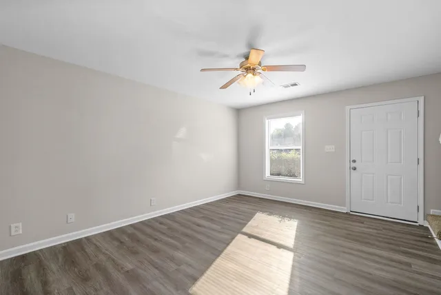 a view of an empty room and wooden floor and a fan