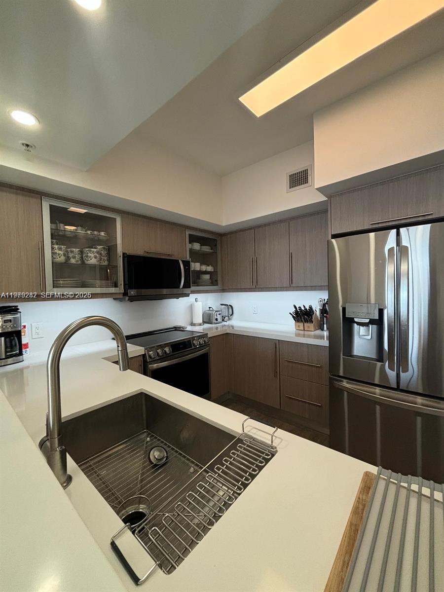 888 Douglas Road, Unit 1002 Coral Gables, FL 33134 - Photo 15 of 34 a kitchen with stainless steel appliances granite countertop a sink stove and refrigerator