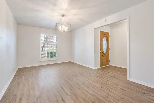 an empty room with wooden floor chandelier and windows