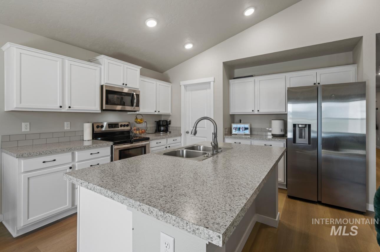 12443 Varga Street Caldwell, ID 83607 - Photo 7 of 27 Kitchen with appliances with stainless steel finishes, lofted ceiling, dark wood-type flooring, light countertops, and white cabinetry