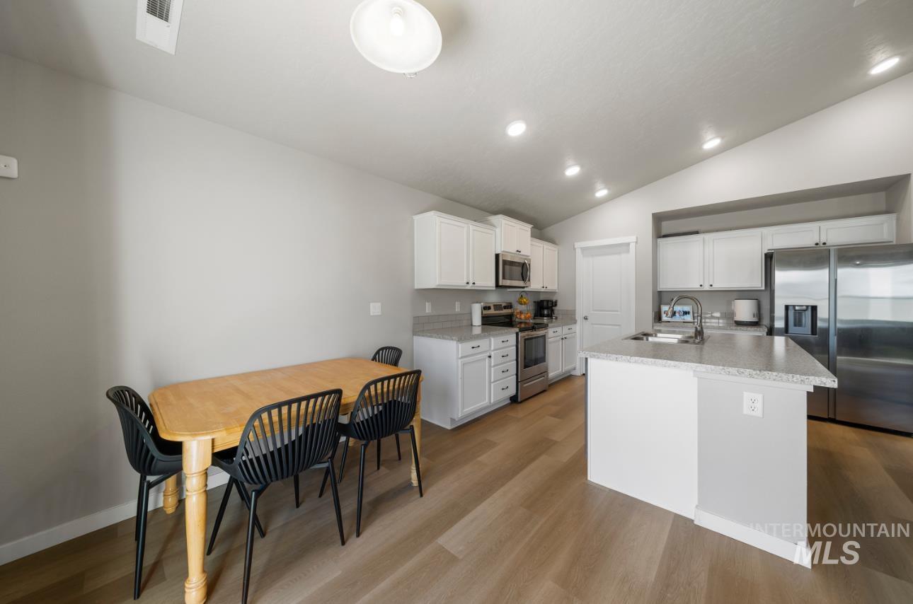 12443 Varga Street Caldwell, ID 83607 - Photo 9 of 27 Kitchen with appliances with stainless steel finishes, lofted ceiling, light wood-style flooring, white cabinetry, and an island with sink