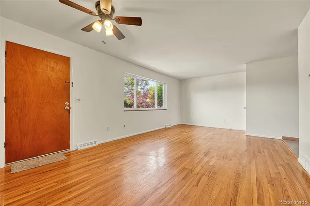 an empty room with wooden floor chandelier fan and windows