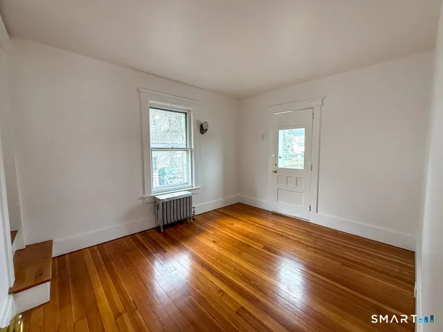 a view of an empty room with wooden floor and a window