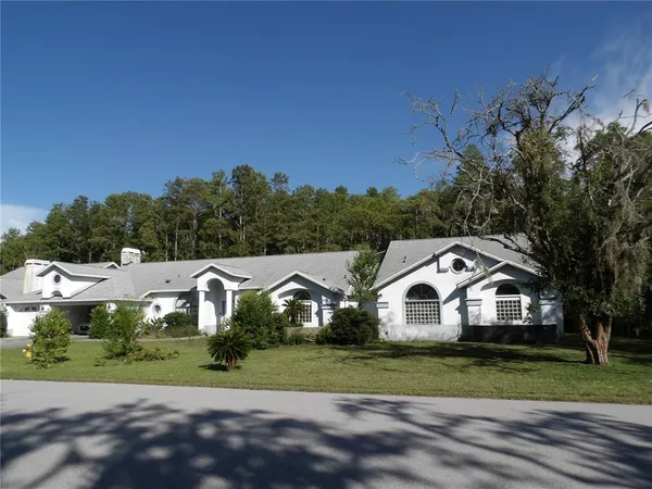 a view of a white house with a big yard and large trees