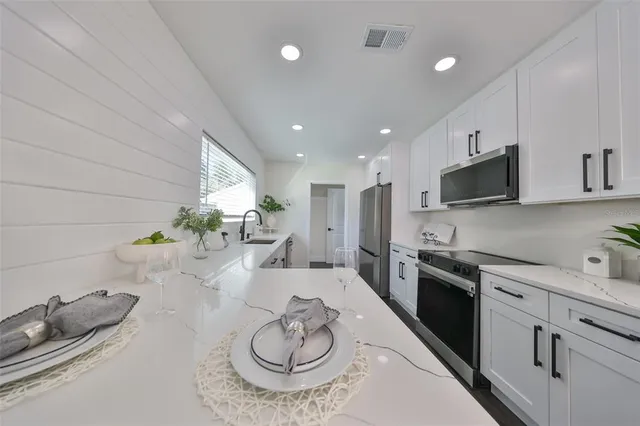 a kitchen with stainless steel appliances kitchen island granite countertop a sink a stove white cabinets and couches with wooden floor