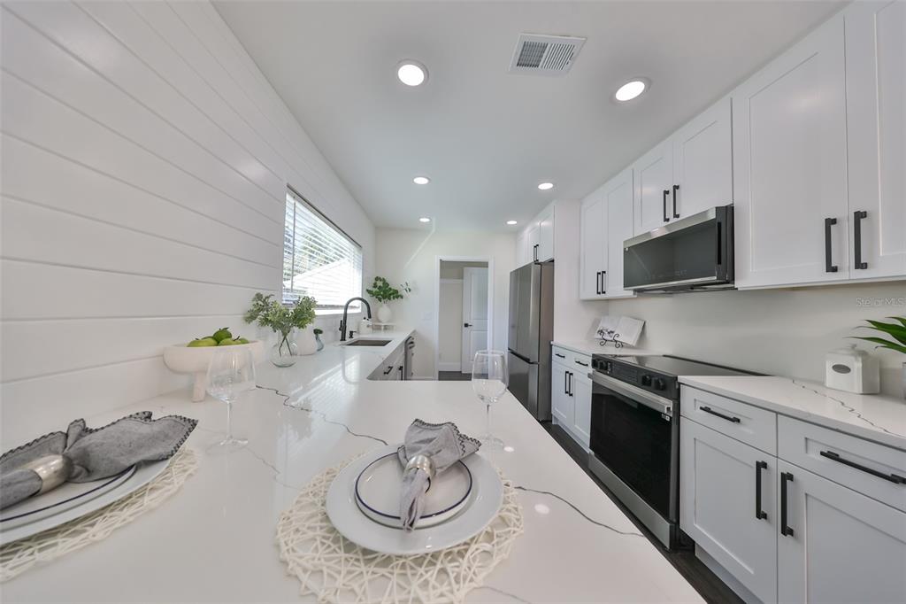 1846 3rd Street South St. Petersburg, FL 33705 - Photo 21 of 40 a kitchen with stainless steel appliances kitchen island granite countertop a sink a stove white cabinets and couches with wooden floor