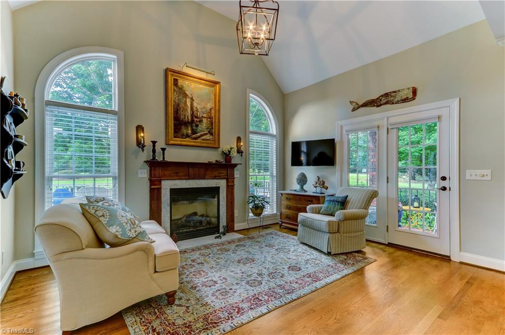 5501 Gray Leigh Drive Oak Ridge, NC 27310 - Photo 11 of 30 The Keeping Room has hardwood floors, gas log fireplace with marble surround & hearth and wood mantel and flanking wall sconces. Large Custom windows have wood blinds and overlook the deck and mature landscaping beyond. Door leads to covered porch. Chandelier not included.