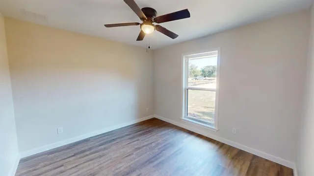 an empty room with wooden floor ceiling fan and windows