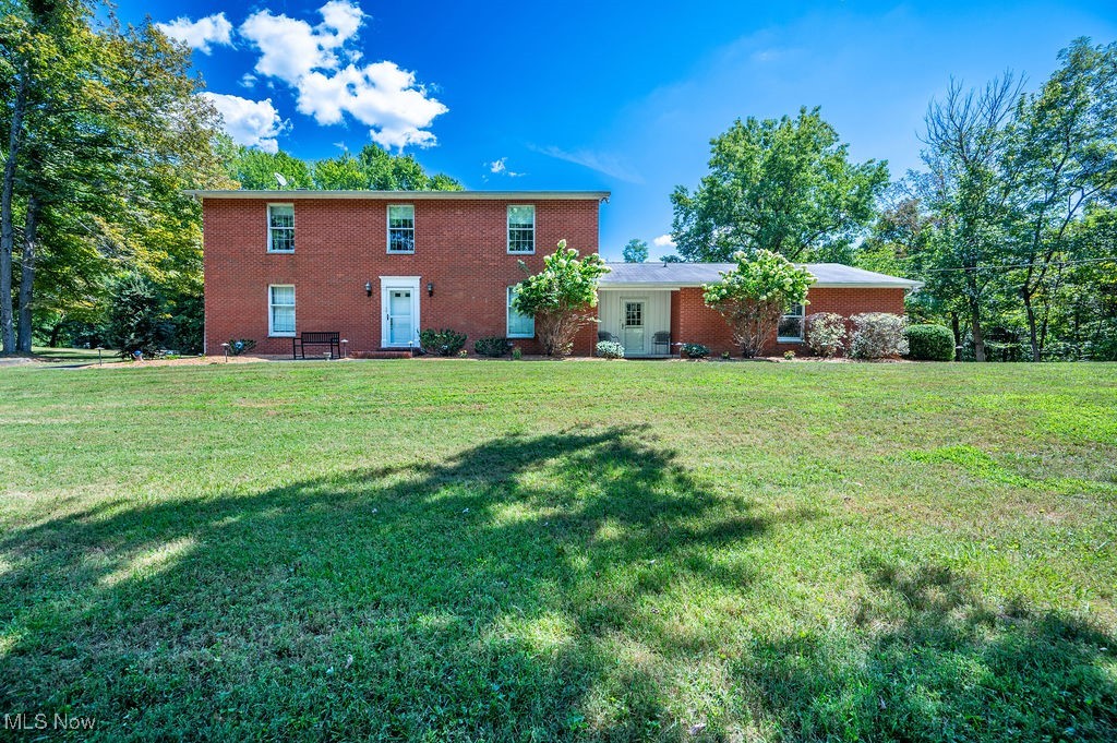 Back of house with a lawn and brick siding