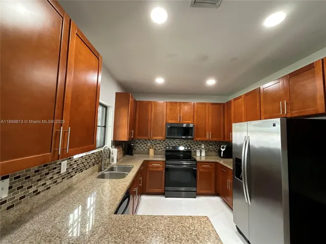 a kitchen with stainless steel appliances granite countertop a refrigerator a stove and a sink