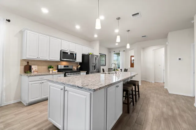 a kitchen with stainless steel appliances granite countertop a sink a stove a refrigerator cabinets and a dining table with wooden floor