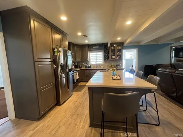 a kitchen with stainless steel appliances kitchen island granite countertop a refrigerator a stove a sink a dining table and chairs with wooden floor