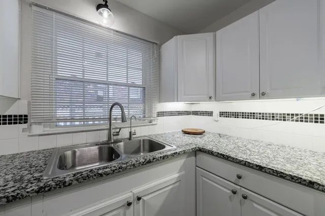 a kitchen with granite countertop a sink and a white wooden cabinets
