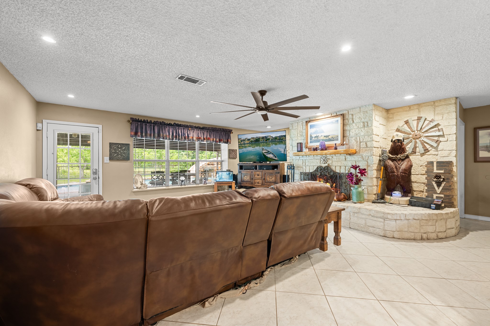 15602 Fir Road Santa Fe, TX 77517 - Photo 15 of 42 Expansive living area featuring a striking stone fireplace, recessed lighting, and oversized windows that fill the space with natural light. The open layout and generous seating area make this room ideal for relaxing or entertaining guests.