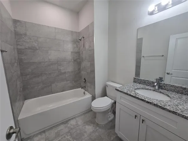 a bathroom with a granite countertop bathtub shower sink vanity mirror and toilet