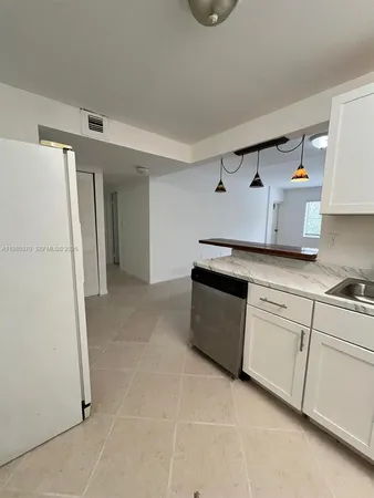 a kitchen with granite countertop a refrigerator a sink and white cabinets