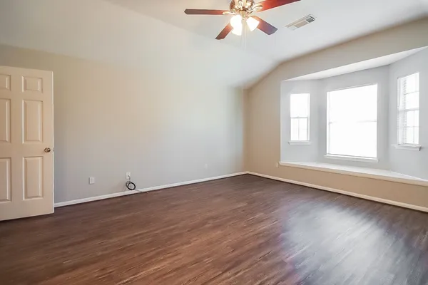 an empty room with wooden floor fan and windows