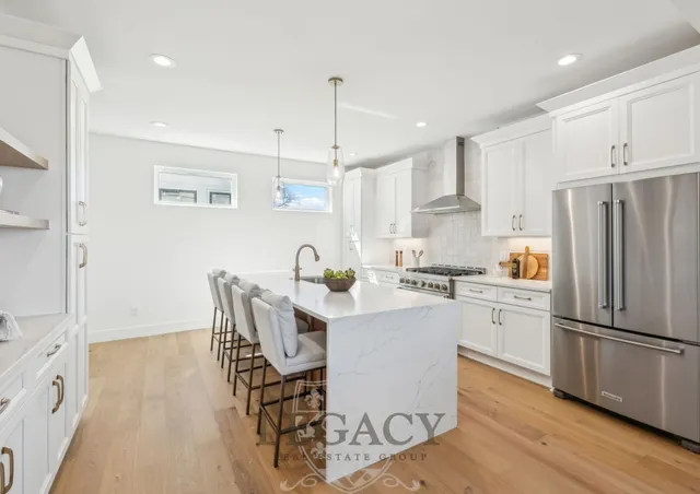 a kitchen with stainless steel appliances a microwave a stove a sink dishwasher a refrigerator and white cabinets with wooden floor