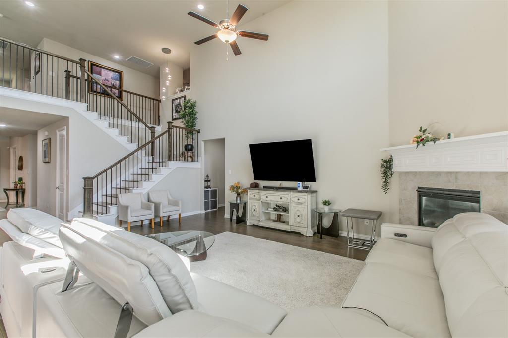 2521 Maidenhair Road Frisco, TX 75033 - Photo 4 of 39 High ceilings featuring a ceiling fan, a fireplace with a stone surround and white mantel, a staircase with dark wood handrails and black metal balusters, dark wood-finish flooring, and recessed lighting