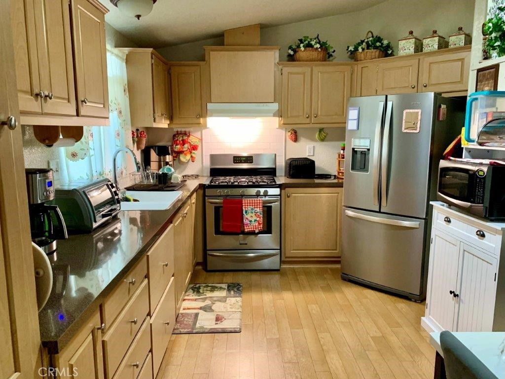 33600 Calimesa Boulevard, Unit 141 Yucaipa, CA 92399 - Photo 4 of 23 a kitchen with stainless steel appliances granite countertop a refrigerator a stove a sink dishwasher and white cabinets with wooden floor