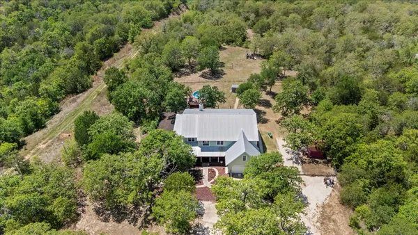 an aerial view of a house with outdoor space and trees all around