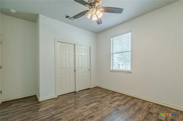 an empty room with wooden floor chandelier fan and windows