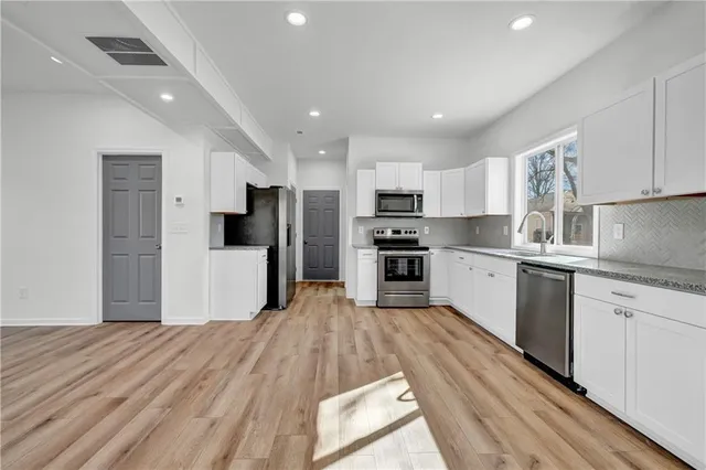 a kitchen with stainless steel appliances kitchen island granite countertop a refrigerator sink and white cabinets
