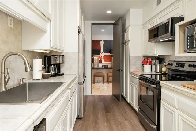a kitchen with stainless steel appliances granite countertop a refrigerator a stove top oven a sink dishwasher and white cabinets with wooden floor
