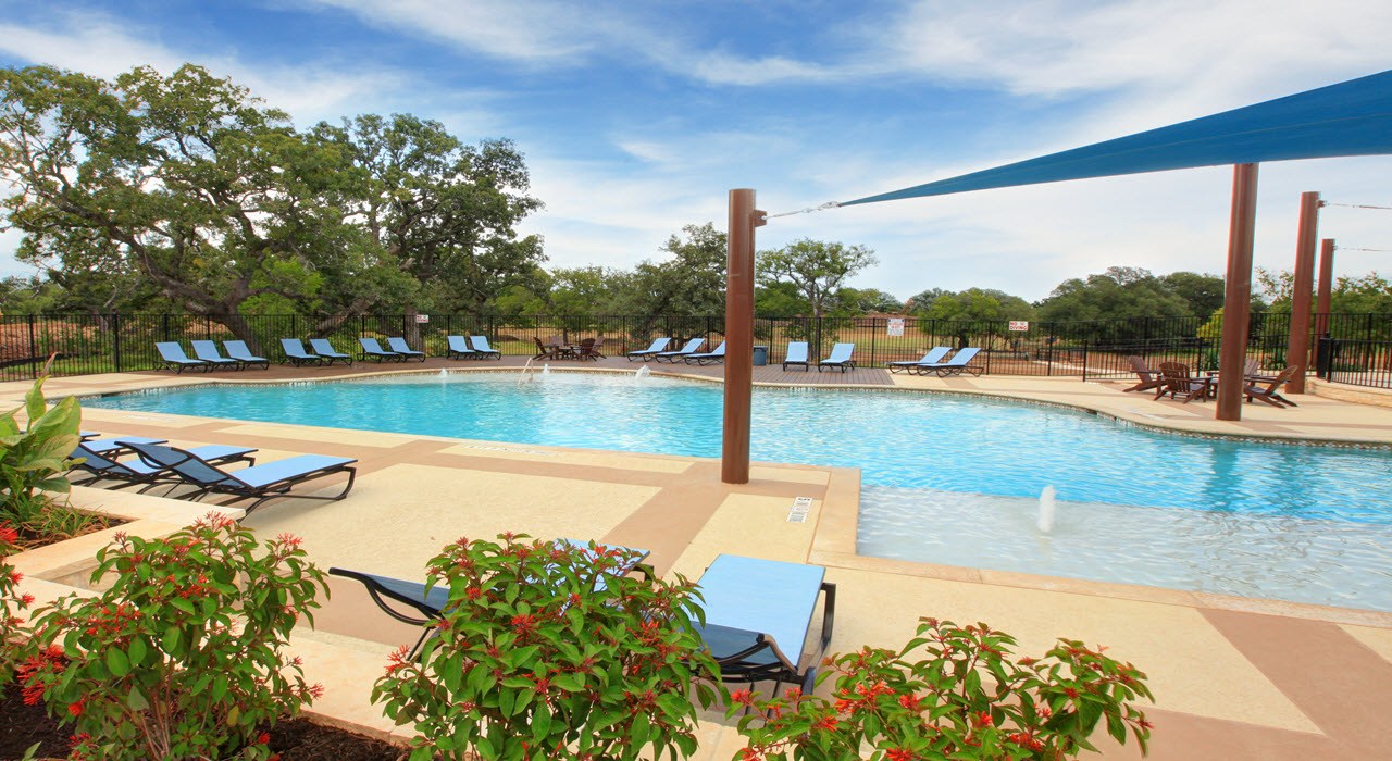 19521 Domino Champ Road Pflugerville, TX 78660 - Photo 5 of 9 An inviting swimming pool area sits surrounded by established trees and concrete sunbathing decks.