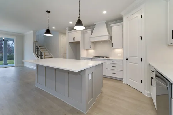 a large white kitchen with stainless steel appliances kitchen island granite countertop a stove a sink a refrigerator and white cabinets with wooden floor