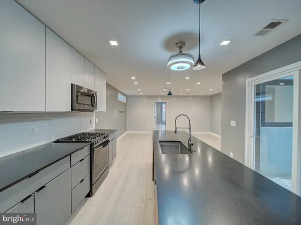 a view of a kitchen with kitchen island stainless steel appliances a stove a sink a oven and a dining table with wooden floor