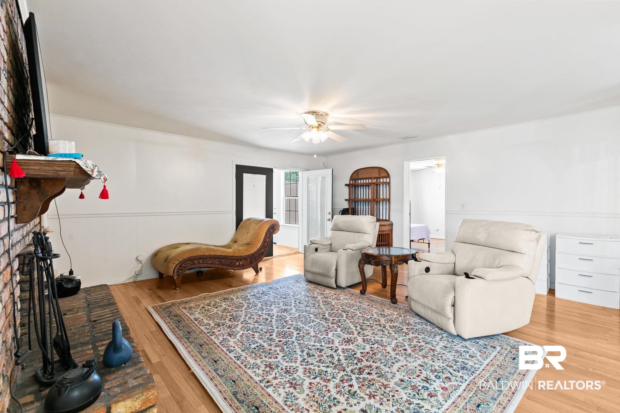 927 Cleveland Road Saraland, AL 36571 - Photo 29 of 80 Living area featuring light wood-finish flooring, white walls with wainscoting, a brick fireplace with a wood mantel, and a ceiling fan with light fixture
