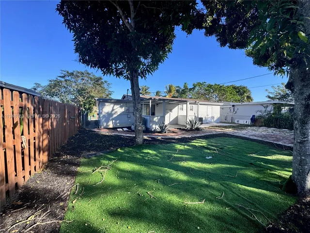 a view of a backyard with table and chairs plants and large trees