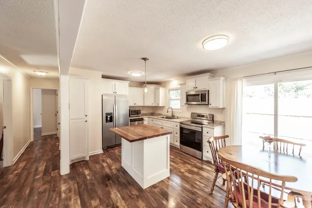 a kitchen with stainless steel appliances kitchen island granite countertop a stove top oven a sink a refrigerator white cabinets and wooden floor
