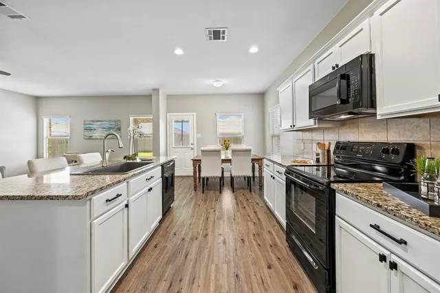 a large kitchen with stainless steel appliances granite countertop a stove top oven a sink dishwasher and white cabinets with wooden floor