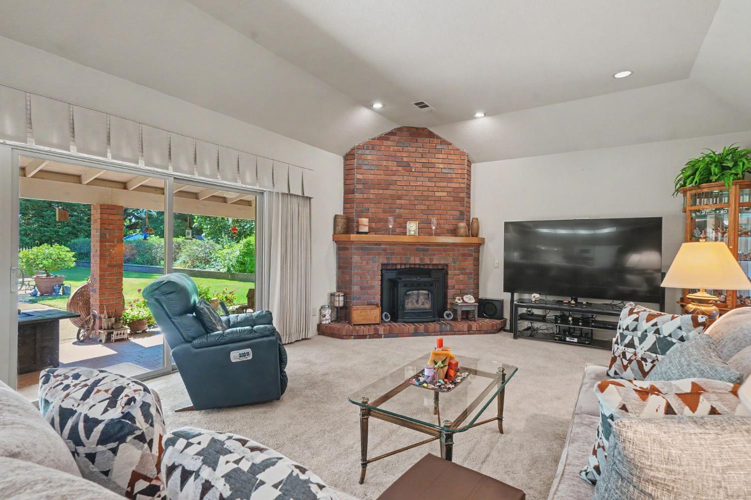 9069 Bader Road Elk Grove, CA 95624 - Photo 4 of 70 Spacious living area featuring a brick fireplace with wood mantel, vaulted ceiling, recessed lighting, and sliding glass doors opening to an outdoor patio with a manicured lawn