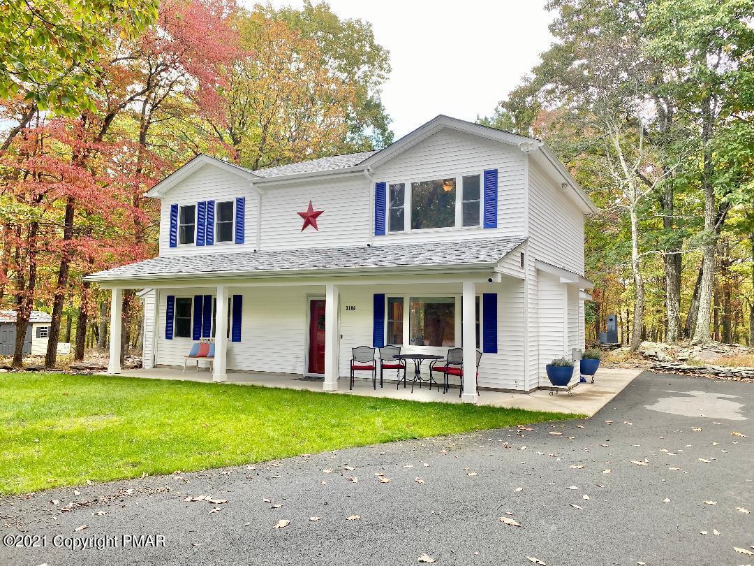 a view of a white house with large windows and a large tree with plants and large trees