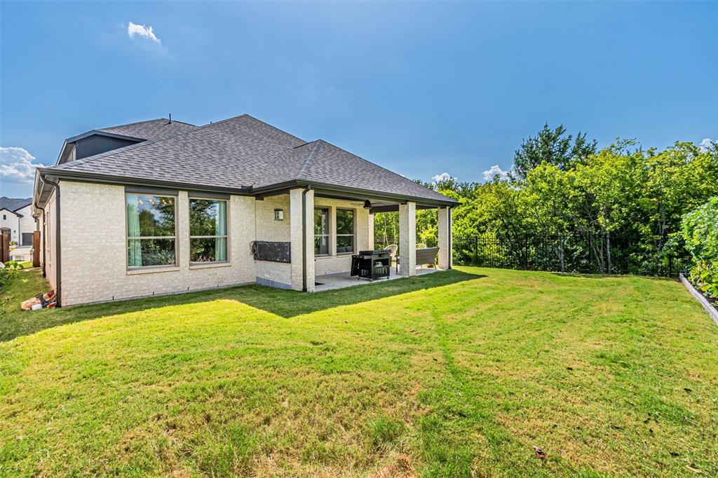 1070 Adair Road Prosper, TX 75078 - Photo 34 of 40 Spacious backyard featuring a covered patio, extensive lawn area, mature perimeter trees, light brick exterior, and dark shingle roofing