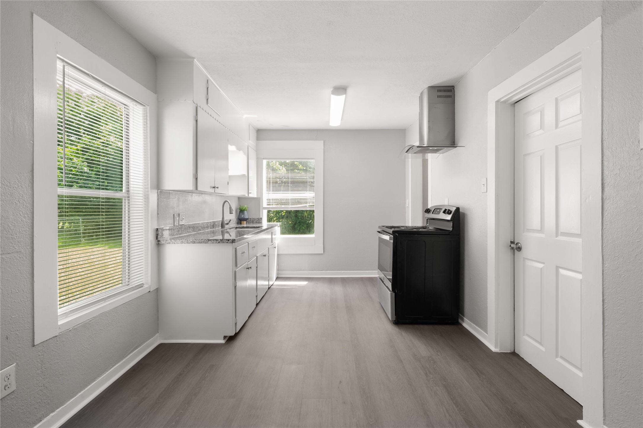 9210 Compton Street Houston, TX 77016 - Photo 15 of 50 Bright and airy kitchen featuring sleek gray flooring, modern white cabinetry, and ample natural light from large windows, creating a welcoming culinary space.