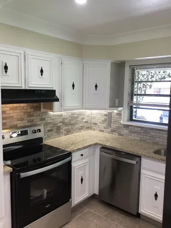 a kitchen with granite countertop white cabinets stainless steel appliances and a window