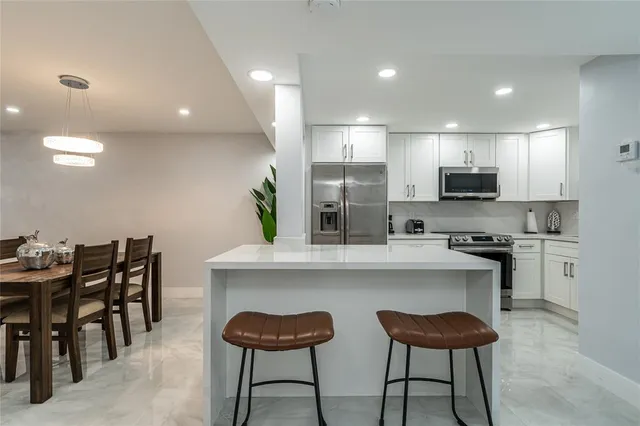 a kitchen with stainless steel appliances kitchen island granite countertop a refrigerator and a stove top oven with white cabinets