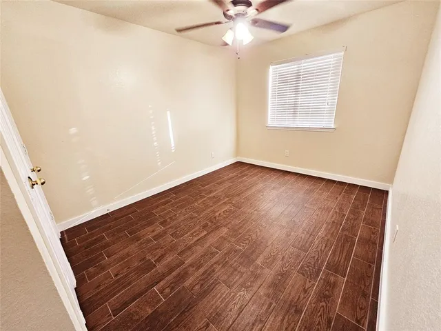 an empty room with wooden floor fan and windows