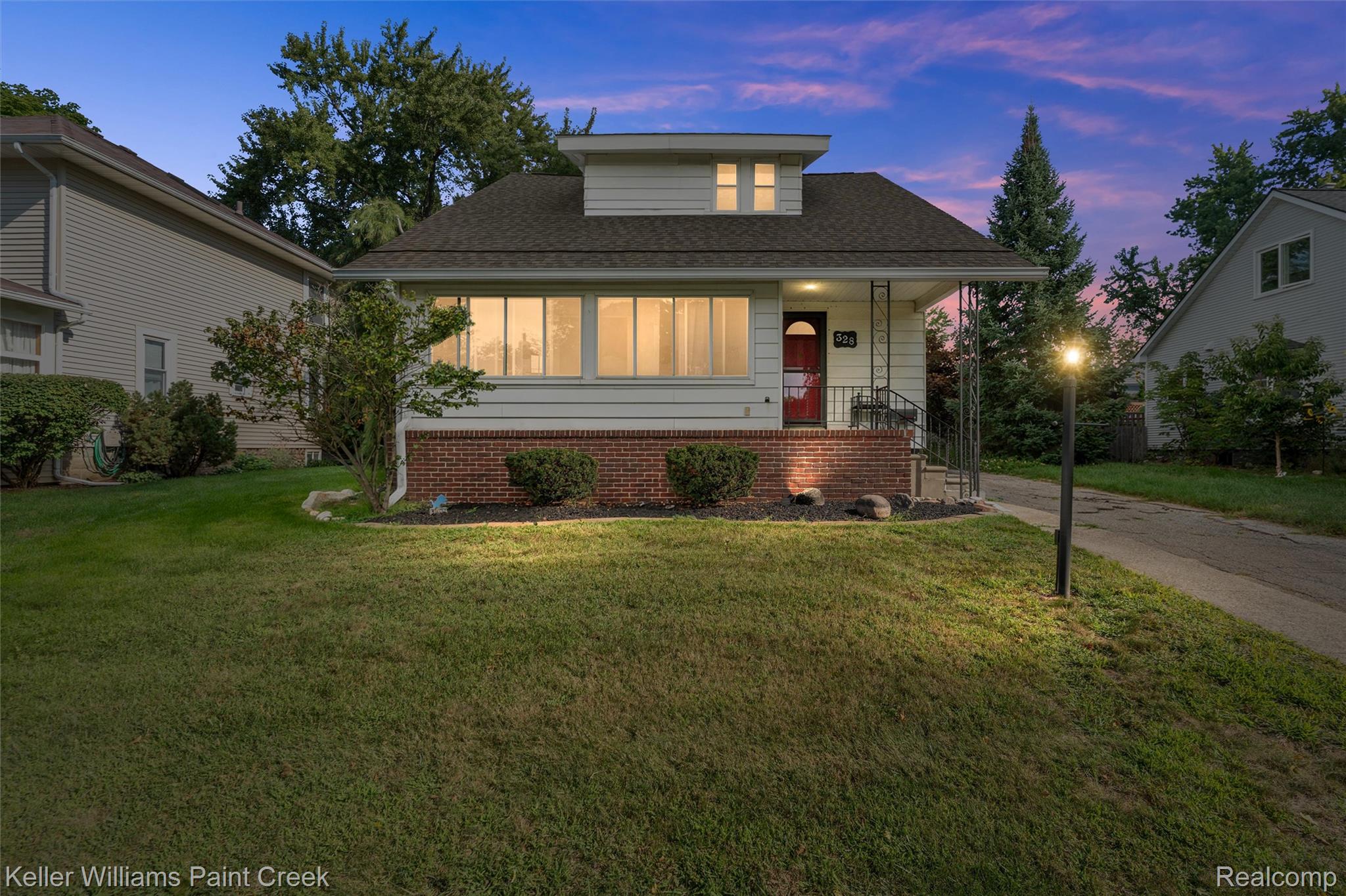 Siding exterior with a brick foundation, covered entry, front lawn, and established landscaping