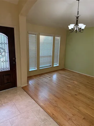 an empty room with wooden floor chandelier and windows