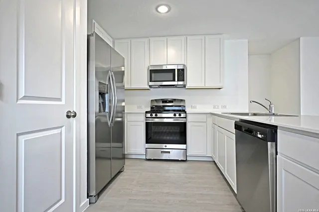 a view of kitchen with stainless steel appliances granite countertop a stove a sink a refrigerator white cabinets and wooden floor